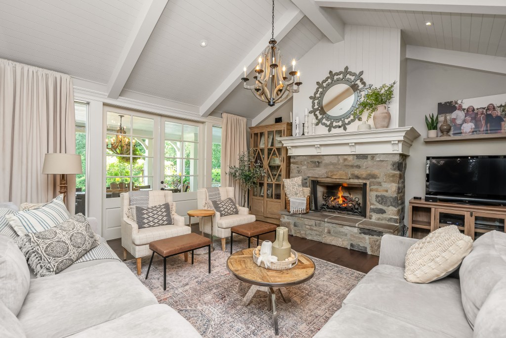 A bright living room scene in Maple Ridge BC features two sofas, a stone fireplace with a fire burning, and a chandelier hanging from the vaulted ceiling.