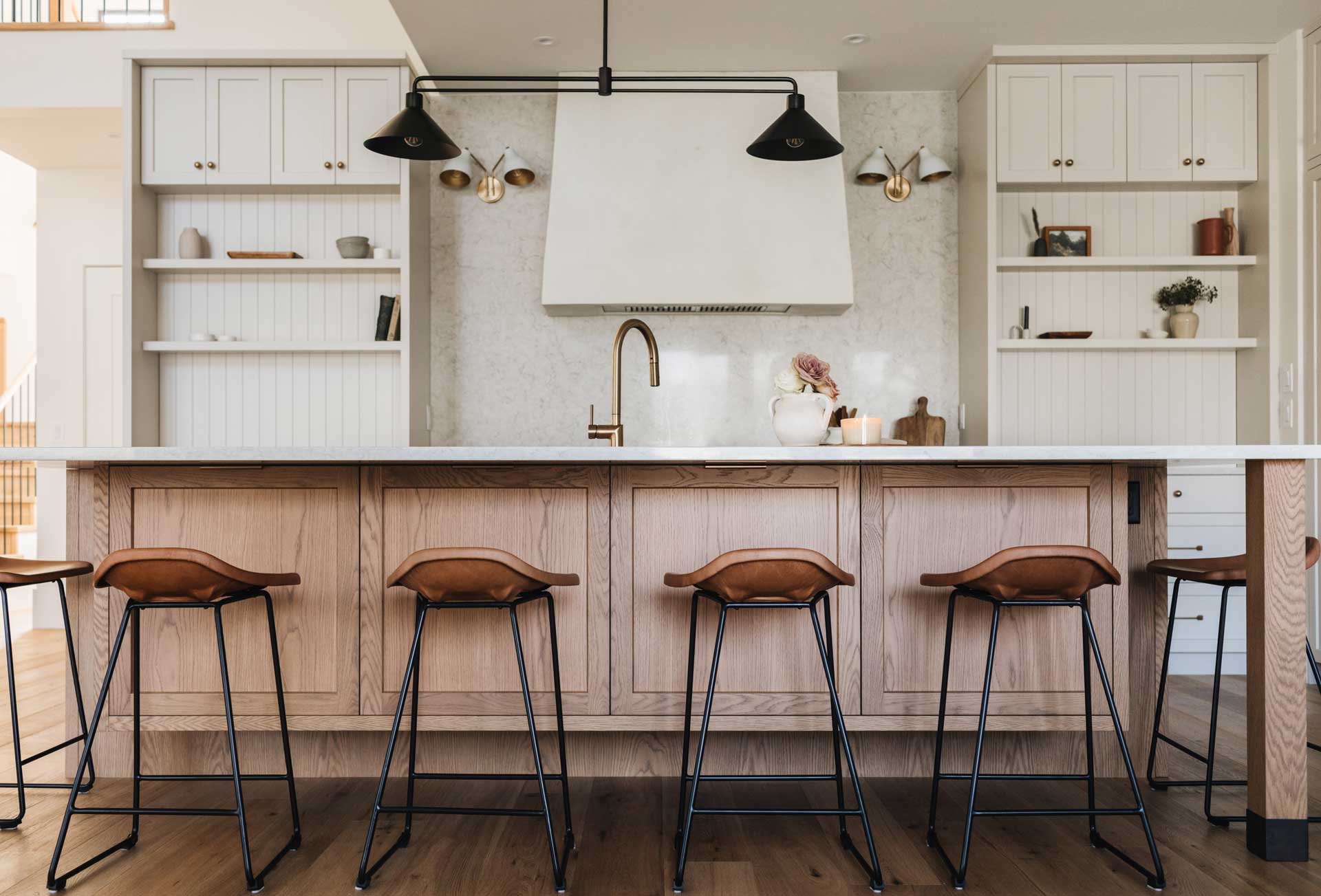 A modern kitchen scene in Maple Ridge BC features a central island with tan leather bar stools and wooden cabinetry, complemented by light countertops and white upper cabinets.
