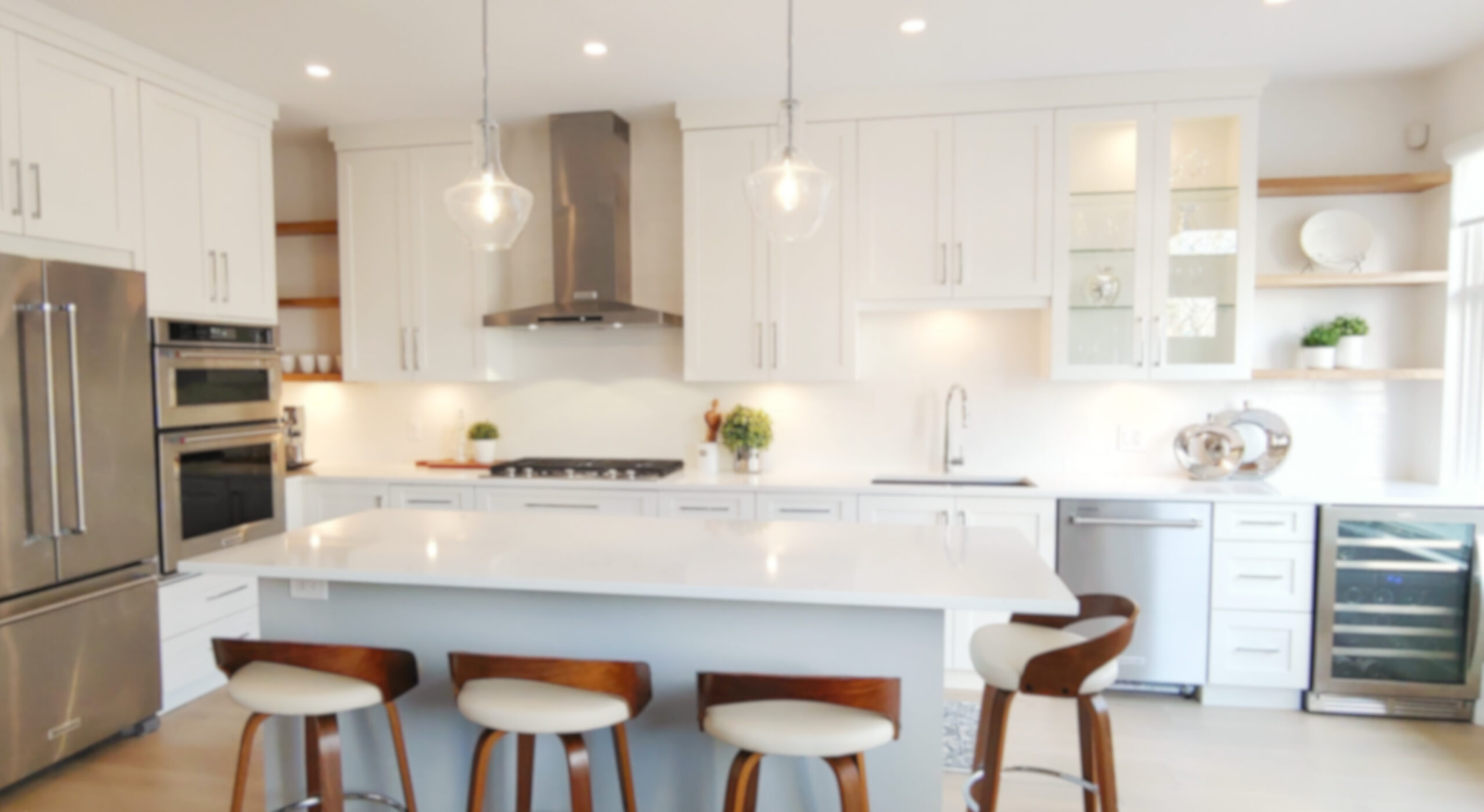 A bright, blurry view of a contemporary kitchen in Maple Ridge, BC, featuring white cabinets, stainless steel appliances, and a large island with seating.