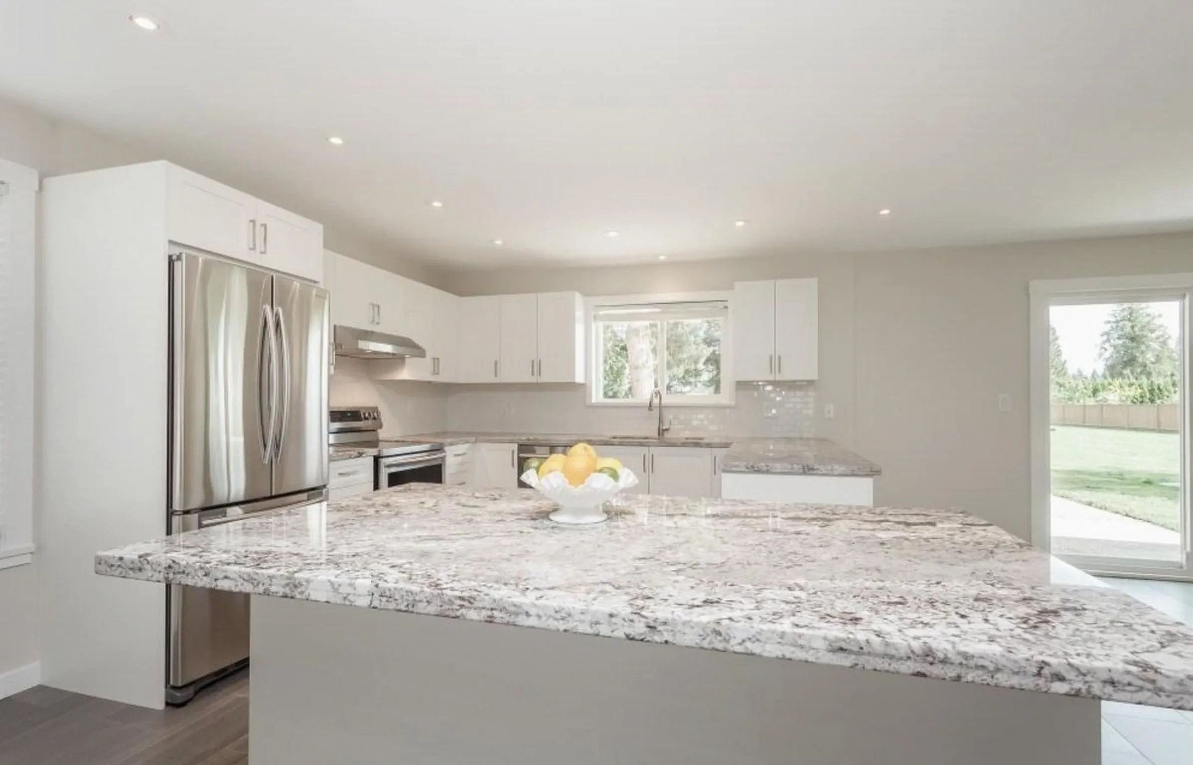 Bright kitchen with a large granite island counter, white cabinets, and stainless steel appliances in Maple Ridge BC.