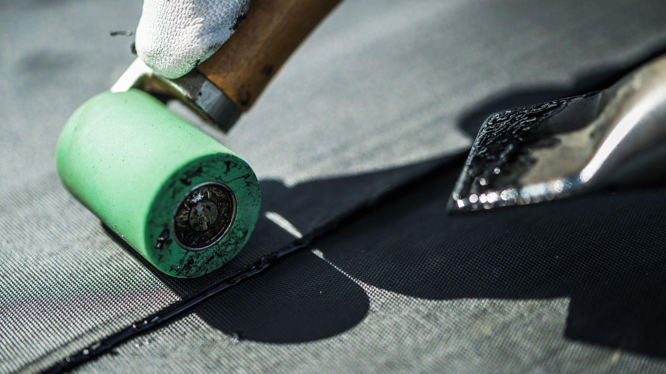 A close-up shows a gloved hand using a seam roller along a black membrane roof in Maple Ridge BC, with a hot air welder in the background.