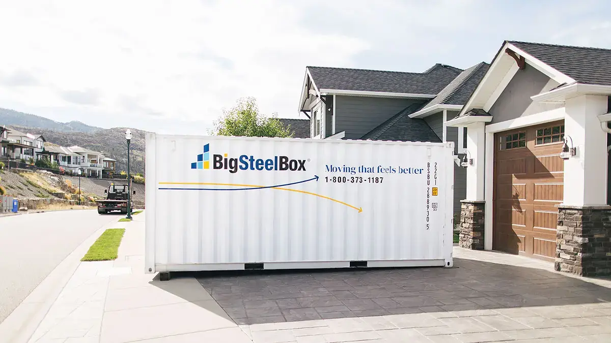 A BigSteelBox shipping container sits on a driveway in Maple Ridge BC, next to a house with a brown garage door.
