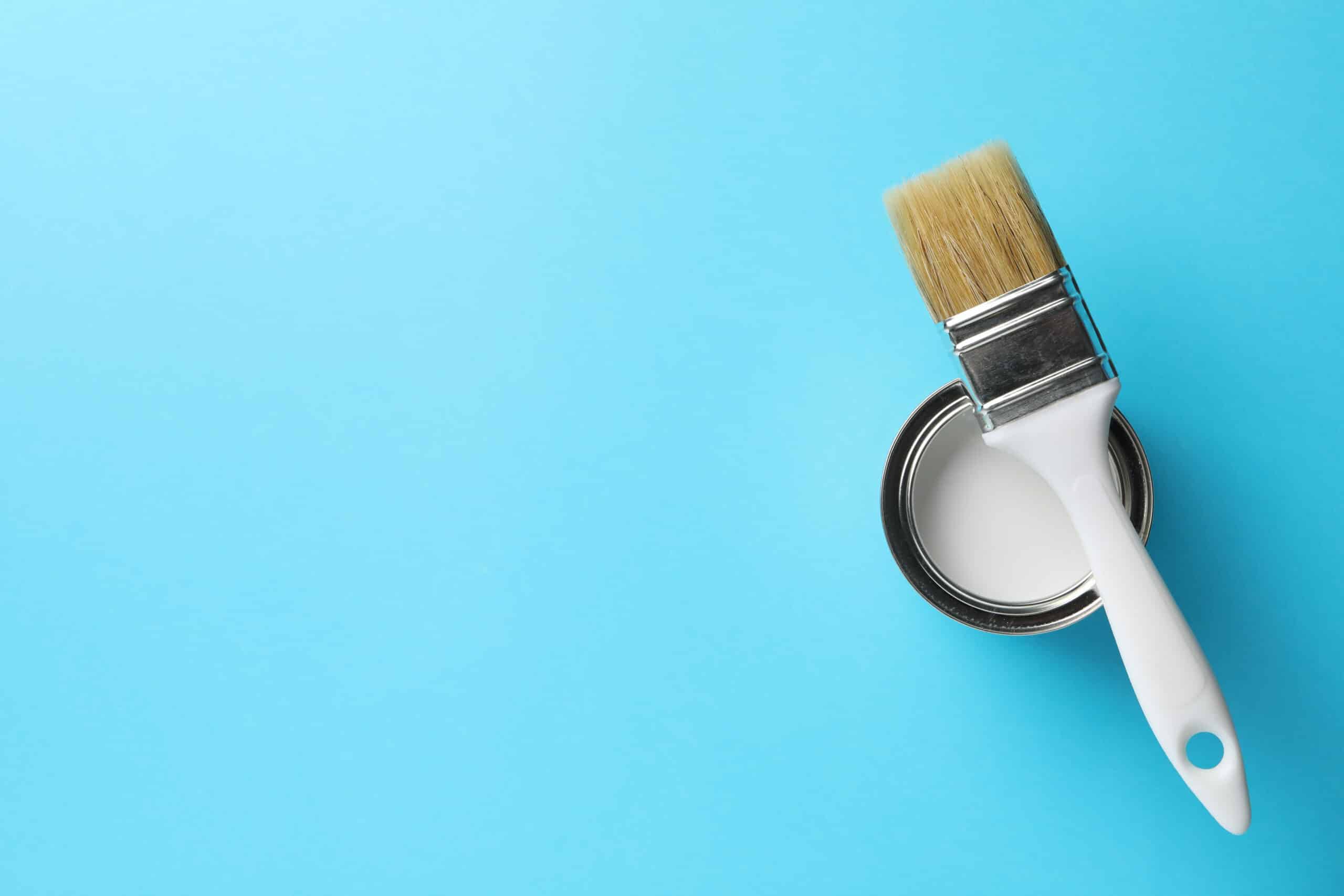 A can of white paint with a brush resting on top, displayed on a light blue background, ready for your next project in Maple Ridge BC.