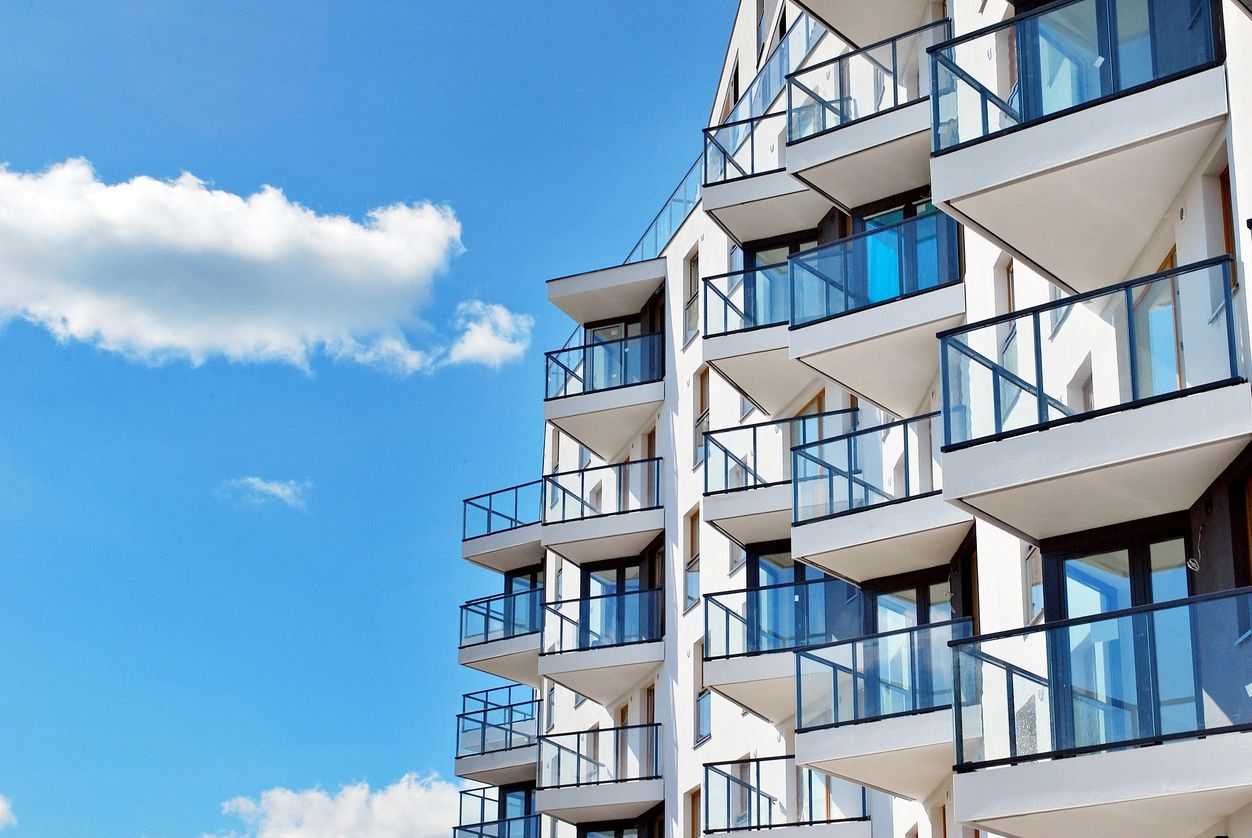 A modern white apartment building in Maple Ridge, BC, with blue glass balconies against a bright blue sky with fluffy clouds.