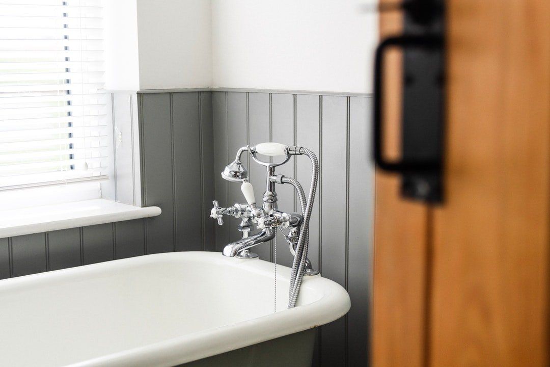 Here is a bathroom scene, maybe somewhere in Maple Ridge BC, with a vintage-style bathtub and chrome faucet fixture, along with a paneled wall and wooden door slightly ajar.