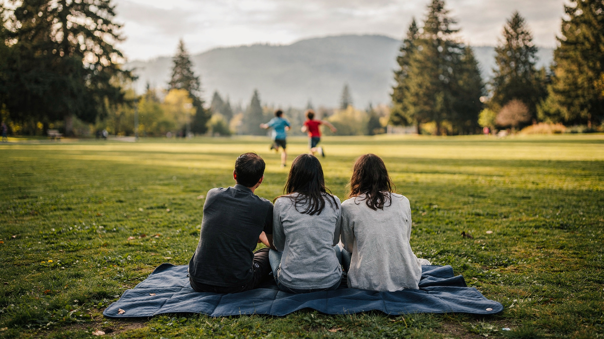 family sitting on a picnic blanket watching children run across a grassy Maple Ridge park