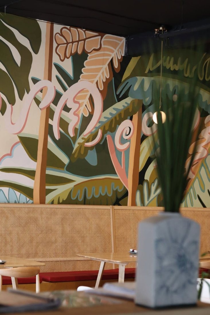 Hand-painted tropical leaf mural above a rattan banquette in the Halina dining room